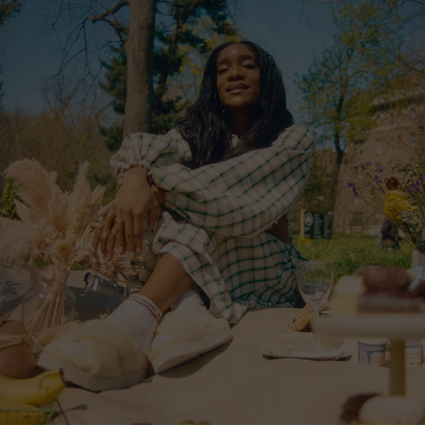 person wearing green dress,sitting on picnic blanket and wearing white UGG slides